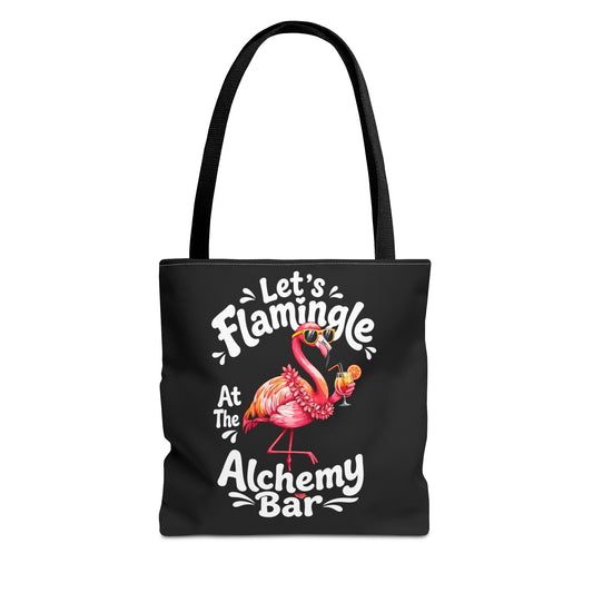 A black tote bag with long shoulder straps, featuring a colorful flamingo graphic and the text 'Let's Flamingle At The Alchemy Bar' printed on the front, shown against a plain white background.