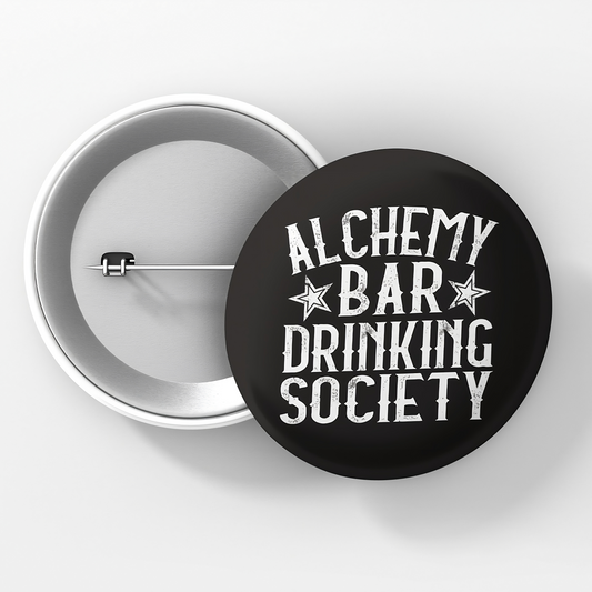A round pinback button with a black background and white text that reads 'ALCHEMY BAR DRINKING SOCIETY' surrounded by three stars.
