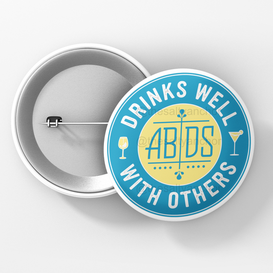 A round pin with a blue background and a yellow center, featuring the text 'ABDS DRINKS WELL WITH OTHERS' and illustrations of drinks.