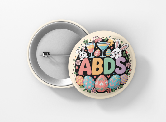 Colorful circular ABDS Easter design featuring pastel block letters surrounded by decorated Easter eggs, flowers, and two cute cartoon bunnies holding cocktails, set on a light beige background.